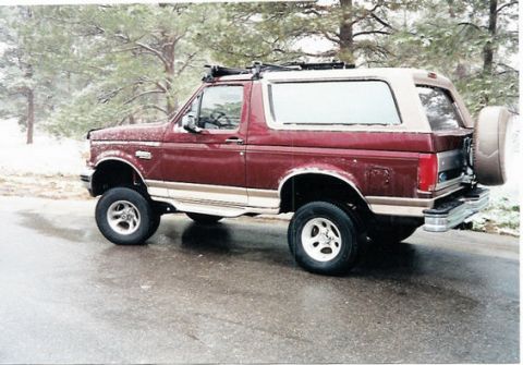 1996 Ford Bronco - A lifted maroon Ford Bronco with a tan top is parked on a wet road during a snowfall.