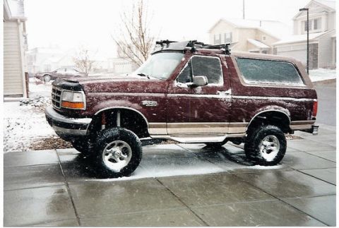 1996 Ford Bronco - Maroon 1996 Ford Bronco with roof rack parked on a wet driveway during snowfall.