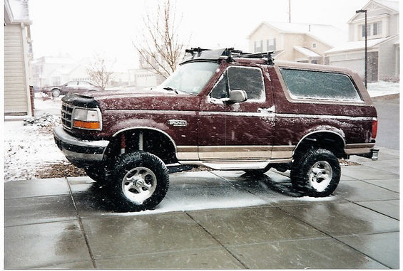 Maroon 1996 Ford Bronco with roof rack parked on a wet driveway during snowfall