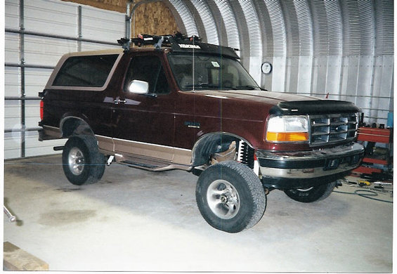 Maroon and tan lifted Ford Bronco with roof rack, parked indoors