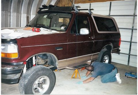 1996 Ford Bronco - A maroon and tan 1996 Ford Bronco is shown with its front end lifted for suspension work.