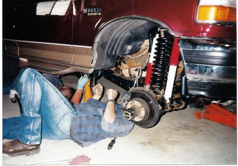1996 Ford Bronco - Mechanic works on the suspension of a maroon 1996 Ford Bronco, with the front wheel removed.