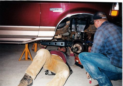 1996 Ford Bronco - Mechanics work on the suspension of a Ford Bronco, which is raised on jack stands.