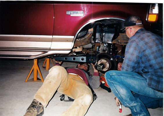 Two guys working under a 1996 Ford Bronco during a lift install