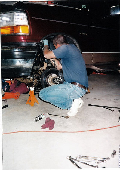 1996 Ford Bronco - Man works on the suspension of a maroon SUV, likely a 1992-1996 Ford Bronco, in a garage setting.