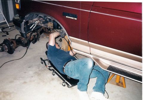 1996 Ford Bronco - Mechanic works on the suspension of a Ford Bronco, with the front axle removed and resting nearby.