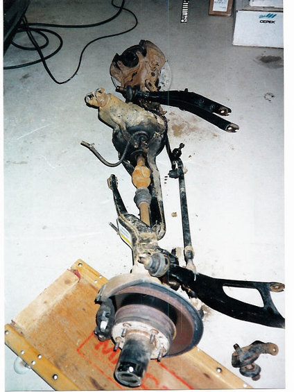 1996 Ford Bronco - Disassembled front suspension components are laid out on a wooden dolly, suggesting a lift installation or repair.