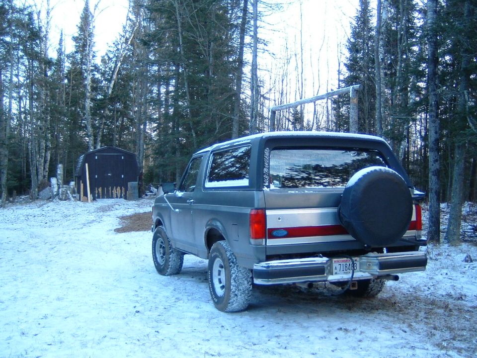 Gray Ford Bronco rear-quarter on snow with roof rack and black-covered rear spare tire