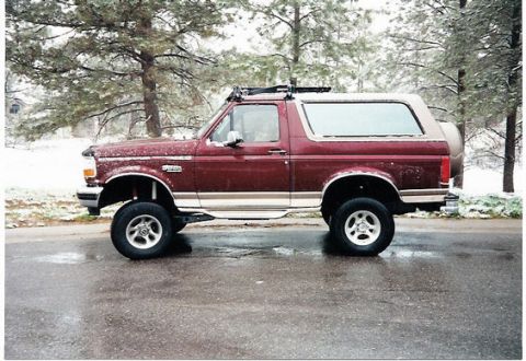 1996 Ford Bronco - A lifted 1996 Ford Bronco sits on a wet road during a light snowfall, its off-road modifications.