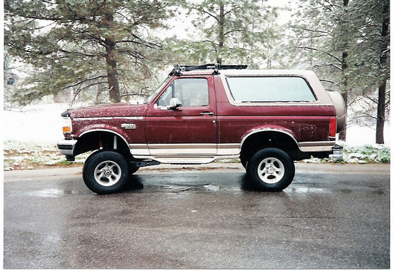 Maroon 1996 Ford Bronco with lifted suspension and roof rack parked on a wet road with snow on the ground