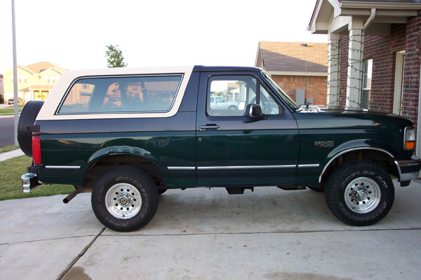 Green Ford Bronco with white removable hardtop parked on a driveway, side view