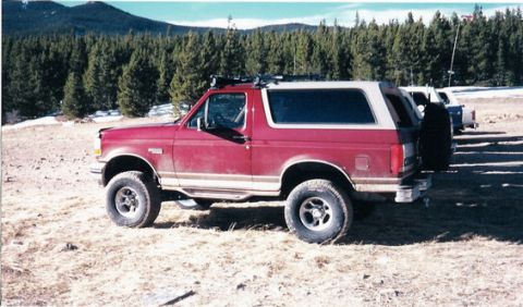 1996 Ford Bronco - A red 1996 Ford Bronco is parked outdoors with a forest and mountains visible in the distance.