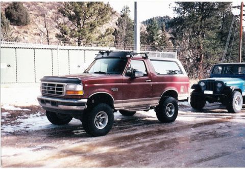 1996 Ford Bronco - A red 1996 Ford Bronco is parked next to a blue Jeep in a snowy lot.
