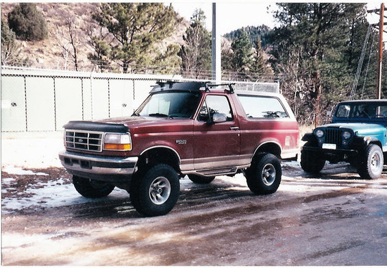 Red 1996 Ford Bronco parked next to a blue Jeep