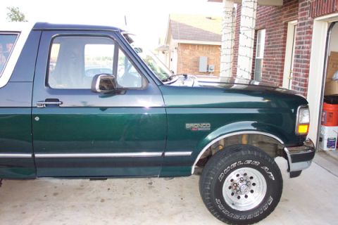 1992 Ford Bronco - Passenger-side profile of a dark green Ford Bronco with a white roof, chrome bodyside molding and 'BRONCO 4x4' fender badging, parked on a…