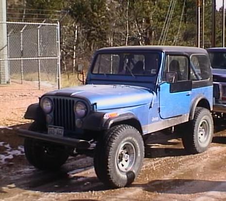 1996 Ford Bronco - A blue Jeep CJ is parked outdoors next to another vehicle, with a chain-link fence and trees visible.