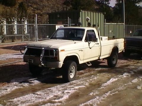 1996 Ford Bronco - A white pickup truck is parked on a lot with patchy snow and dirt, with another dark vehicle visible to the right.