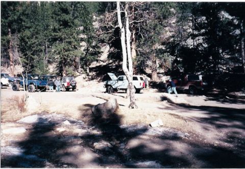 1996 Ford Bronco - Multiple off-road vehicles are parked in a wooded area, with one vehicle's hood open.