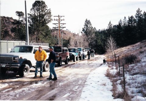 1996 Ford Bronco - A group of Ford Broncos are parked on a dirt road covered in snow and ice, with a line of trees in the background.