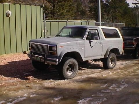 1996 Ford Bronco - A gray Ford Bronco is parked outdoors on a gravel surface, with a second vehicle partially visible to its right.