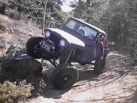 1996 Ford Bronco - A purple Jeep CJ-7 navigates a rocky trail, with its front tire high off the ground.