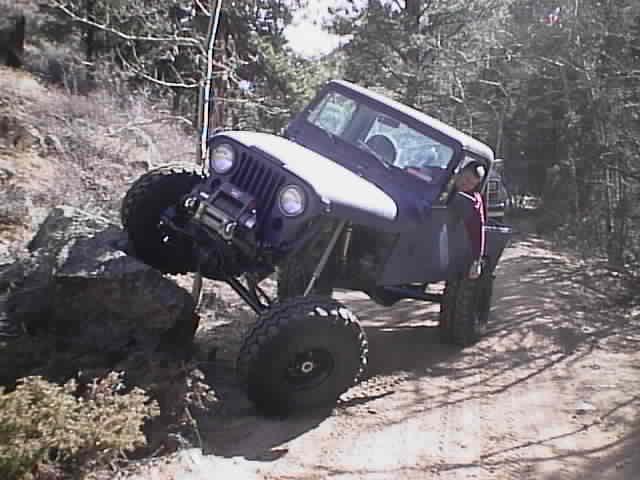 Purple Jeep CJ-7 off-roading over rocks on a dirt path