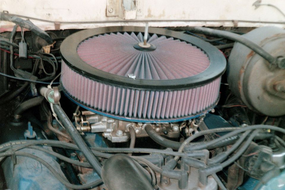 Red K&N-style round air filter on a four-barrel carburetor over a blue Ford V8
