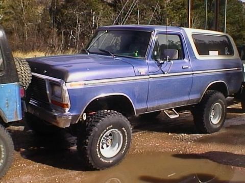 1996 Ford Bronco - A blue Ford Bronco with a white top is parked next to a blue Jeep, showing its lifted suspension and off-road tires.