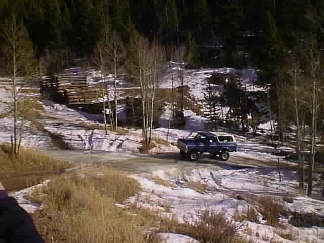 1996 Ford Bronco driving on a dirt road with snow and trees