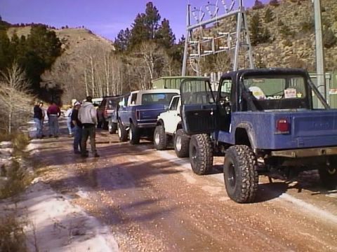 1996 Ford Bronco - Several trucks and SUVs are parked in a line on a dirt road, with a power substation visible.