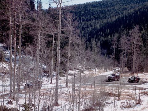 1996 Ford Bronco - Two SUVs are parked on a dirt road surrounded by trees and snow.