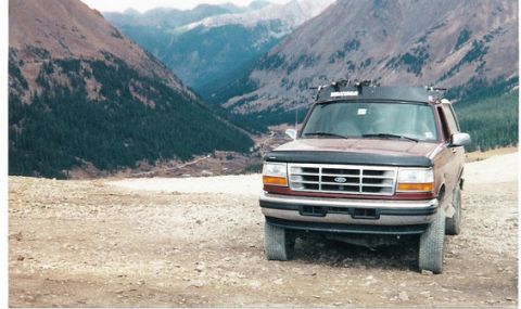 1996 Ford Bronco - 1996 Ford Bronco parked on a dirt road with mountains in the background.
