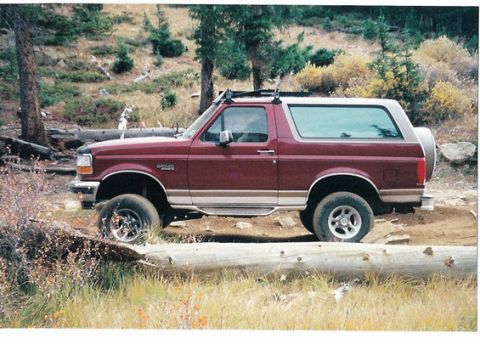 1996 Ford Bronco - A maroon Ford Bronco is parked off-road in a wooded area.