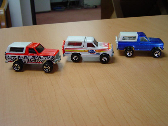 Three die-cast toy Ford Bronco and pickup models lined up on a wood table