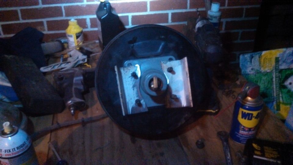 Brake booster assembly with mounting bracket and pushrod. WD-40 can and other tools are visible