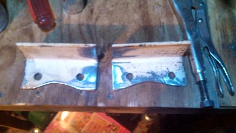 1979 Ford Bronco - Two metal brackets are shown on a workbench, possibly for automotive repair or modification.