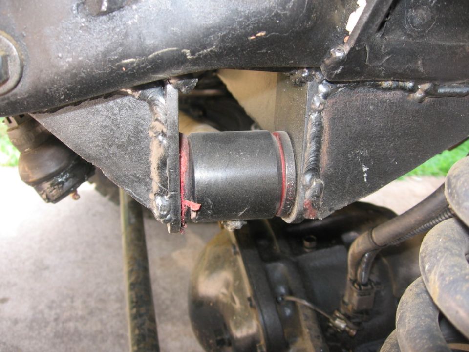 Close-up of a black suspension bushing with red trim, attached to a black metal frame with visible welds