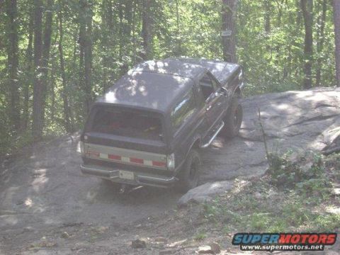 1988 Ford Bronco - Dark SUV with chrome side steps and a silver stripe on the tailgate, navigating a dirt and rock path.