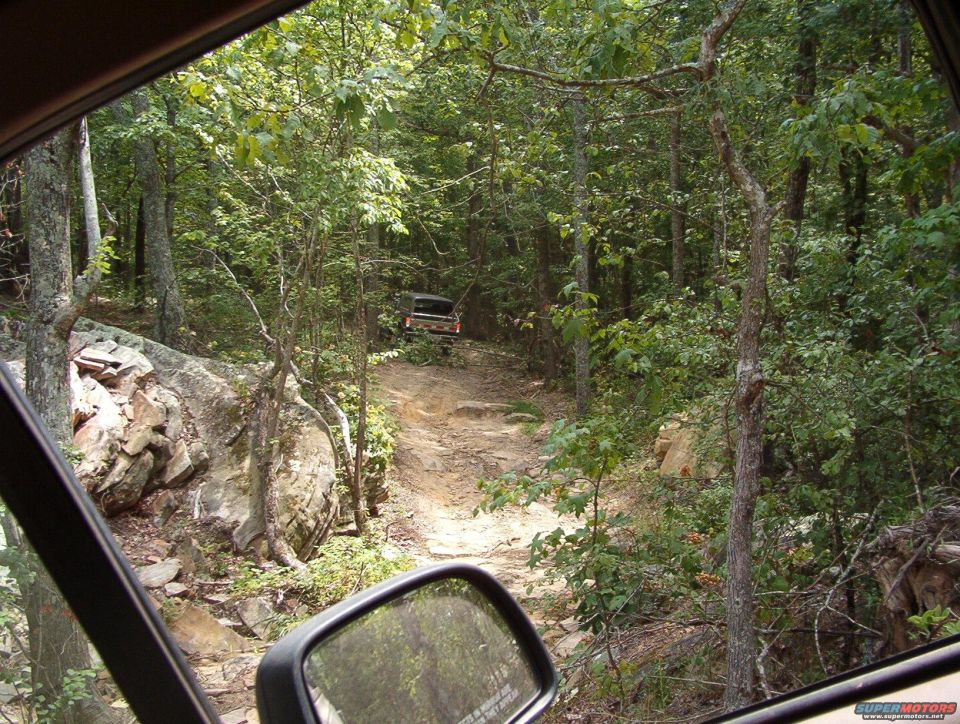 View from inside a vehicle looking out at another vehicle driving up a rocky, wooded trail