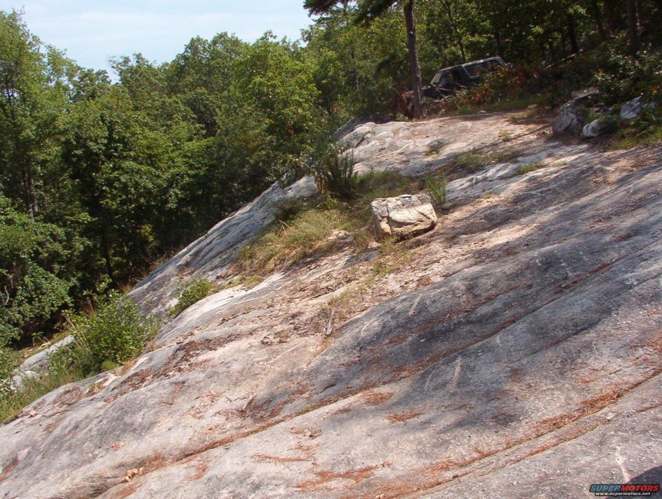 rocky slope with trees and a distant vehicle partially visible
