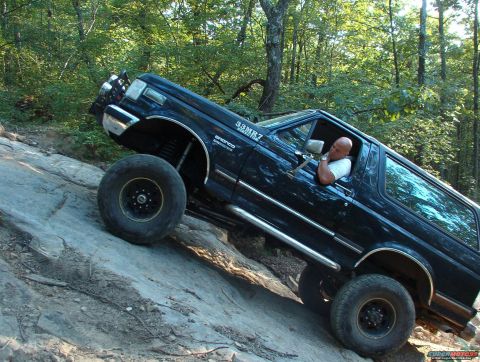 1988 Ford Bronco - A man drives a black Ford Bronco up a steep, rocky incline in a wooded area.