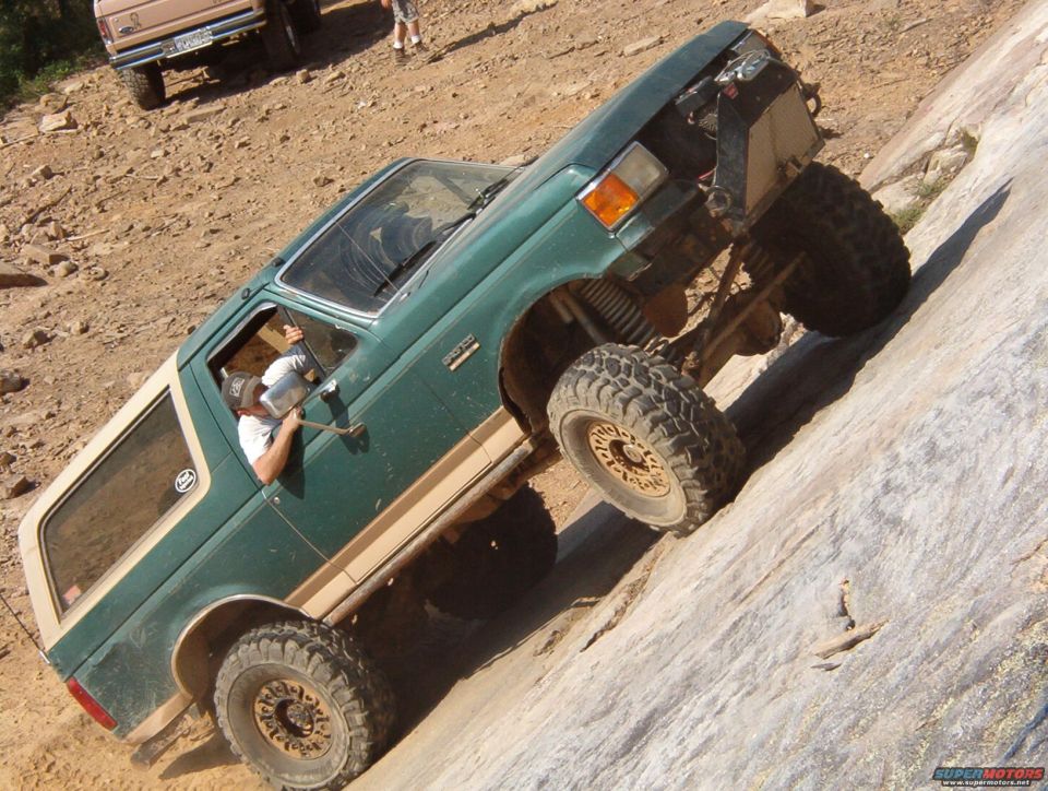 Green Ford Bronco with tan trim climbing a rock face, front wheel elevated