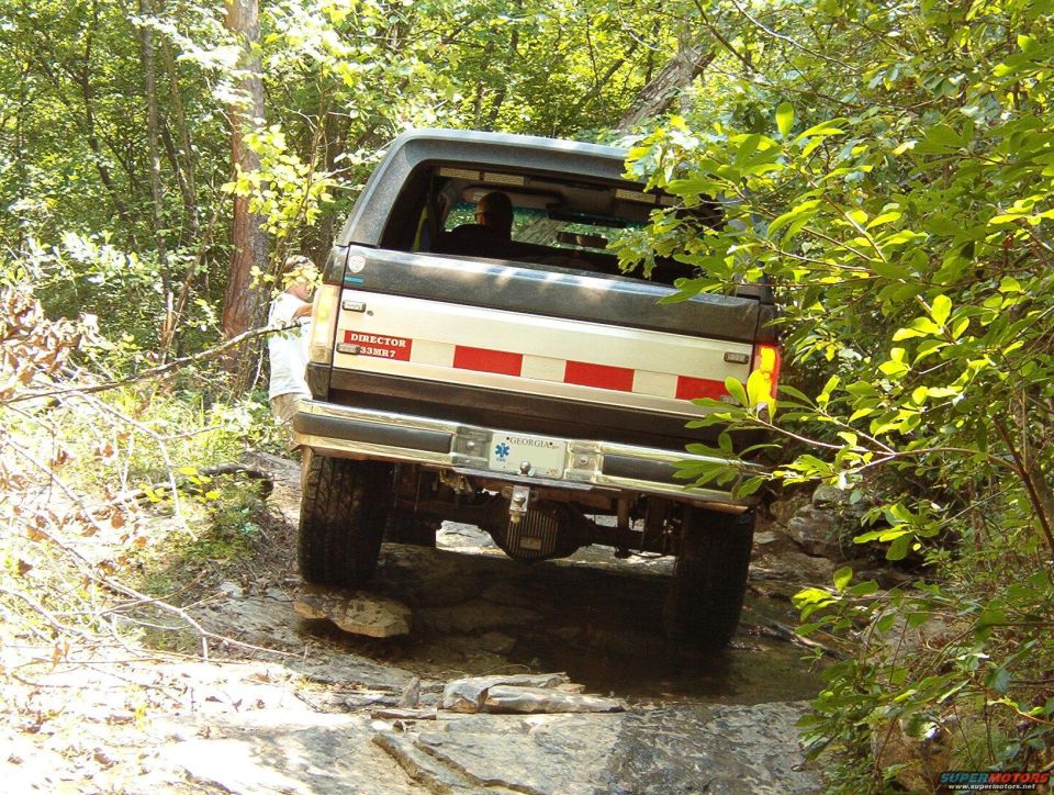 1988 Ford Bronco navigating a rough, wooded trail from the rear