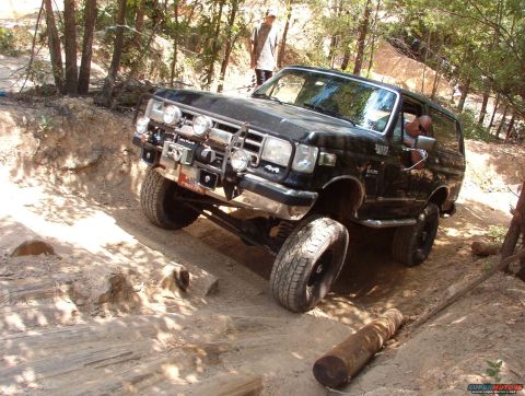 1988 Ford Bronco - Black Ford Bronco tackling a challenging off-road obstacle on a dirt path.