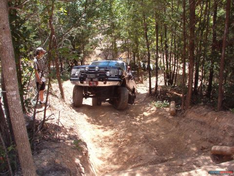 1988 Ford Bronco - A lifted truck navigates a wooded trail with a person observing from the side.