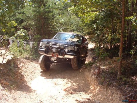 1988 Ford Bronco - This modified SUV navigates a challenging off-road course with checkered flags in the background.