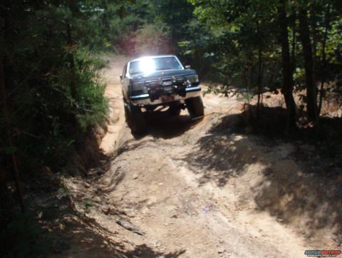 1988 Ford Bronco - Ford Bronco navigates a challenging off-road path through a wooded area.