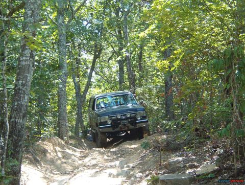 1988 Ford Bronco - A dark SUV navigates a steep, wooded trail with visible tire tracks.