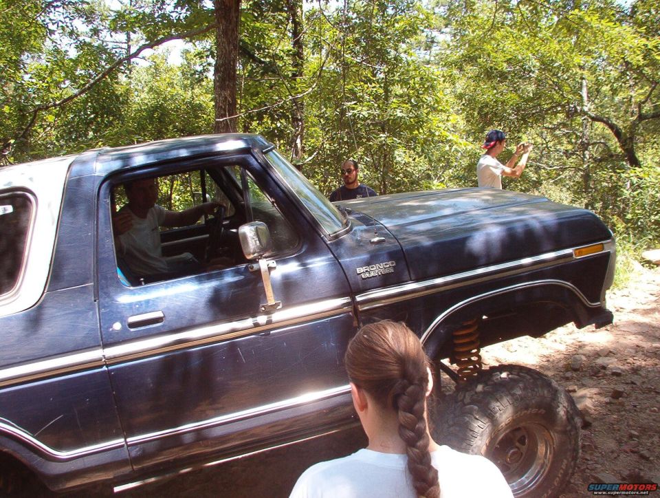 Dark blue Ford Bronco with white top, side view, lifted suspension