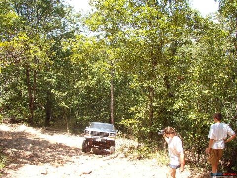 1988 Ford Bronco - 1988 Ford Bronco navigating a dirt road surrounded by trees, with two onlookers present.